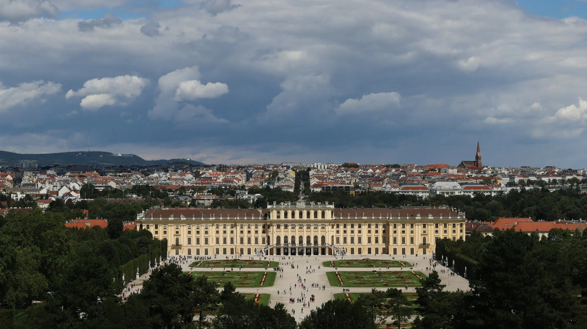 Panoramic view of Schönbrunn Palace, a yellow Baroque palace with Vienna cityscape in the background.